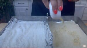 Woman seasoning flour and breadcrumbs for cooking on a foil-lined baking sheet in a kitchen.